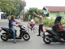 POLISI PENOLONG BHABINKAMTIBMAS BANTU MENYEBRANGKAN MASYARAKAT DI PERSIMPANGAN JALAN